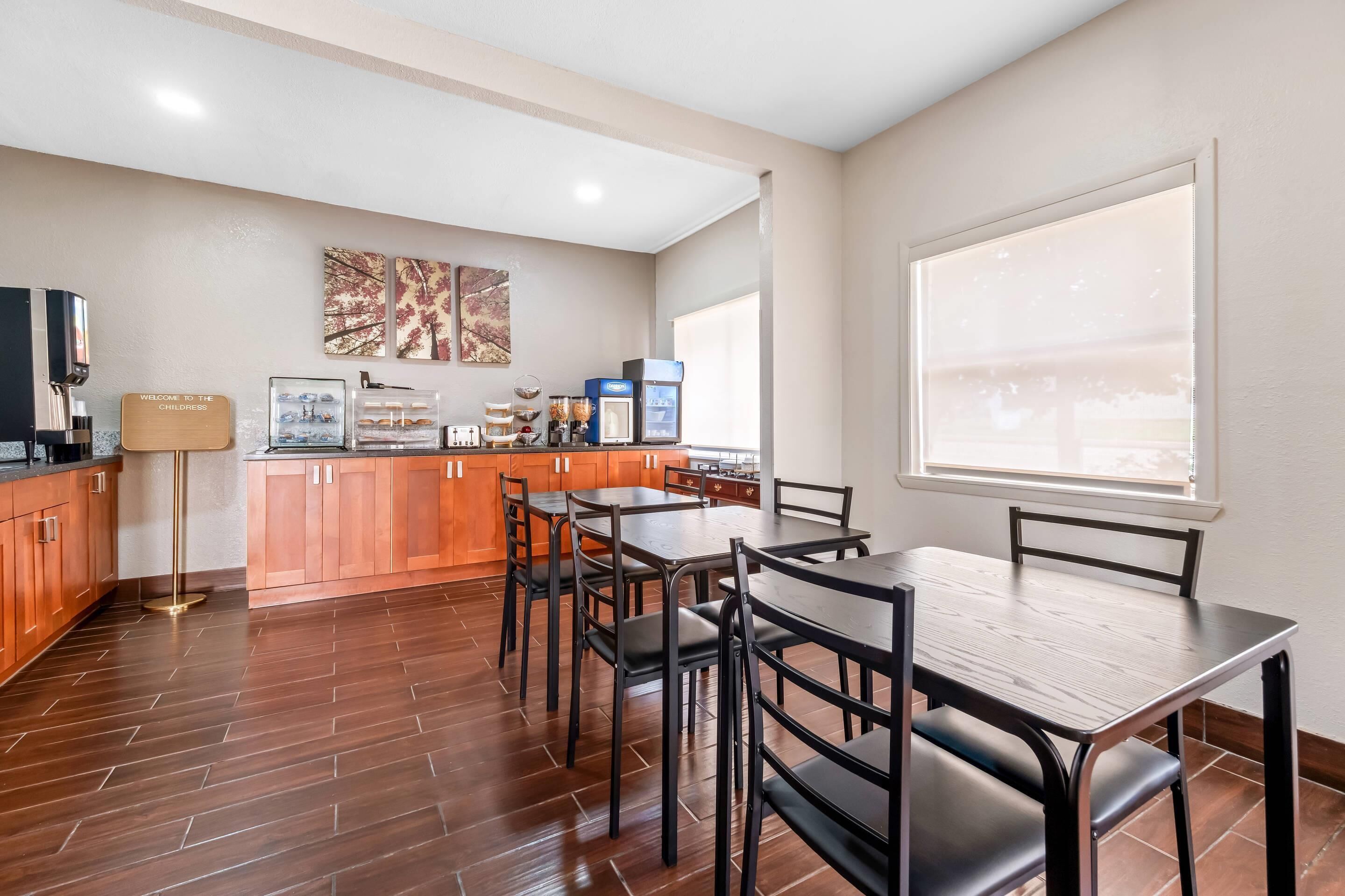 A modern kitchen with wooden cabinets, a coffee machine, and a dining area with a table and chairs.