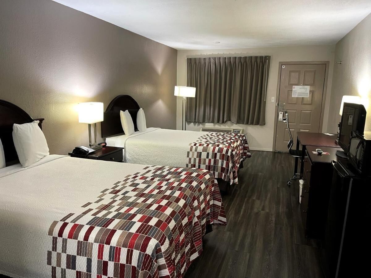 A hotel room with two beds, a desk, a television, and a door.
