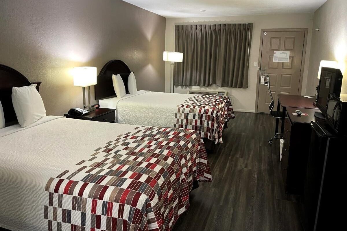 A hotel room with two beds, a desk, a television, and a door.