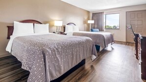 A hotel room with two beds, a desk, a chair, a window with curtains, and a door.