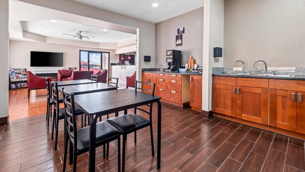 A spacious living area with a dining table and chairs, a kitchen with wooden cabinets, and a flat-screen TV mounted on the wall.