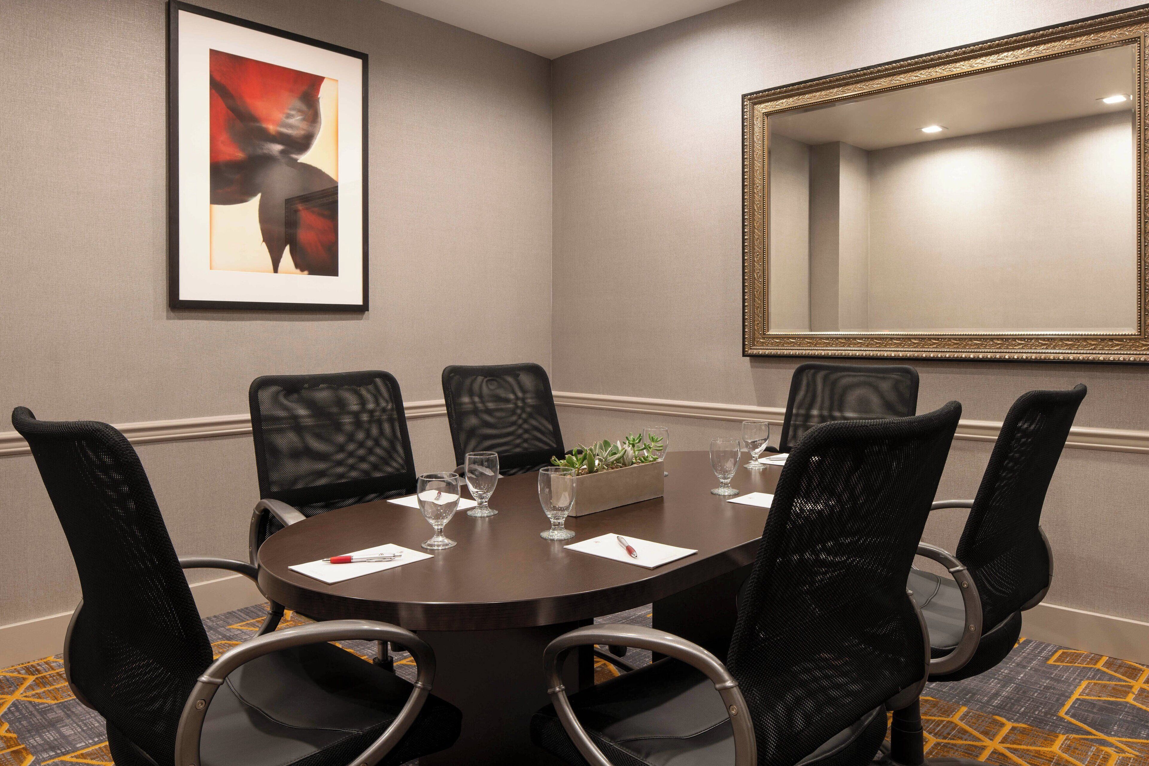 A conference room with a round table, six chairs, a large mirror, and a framed artwork on the wall.
