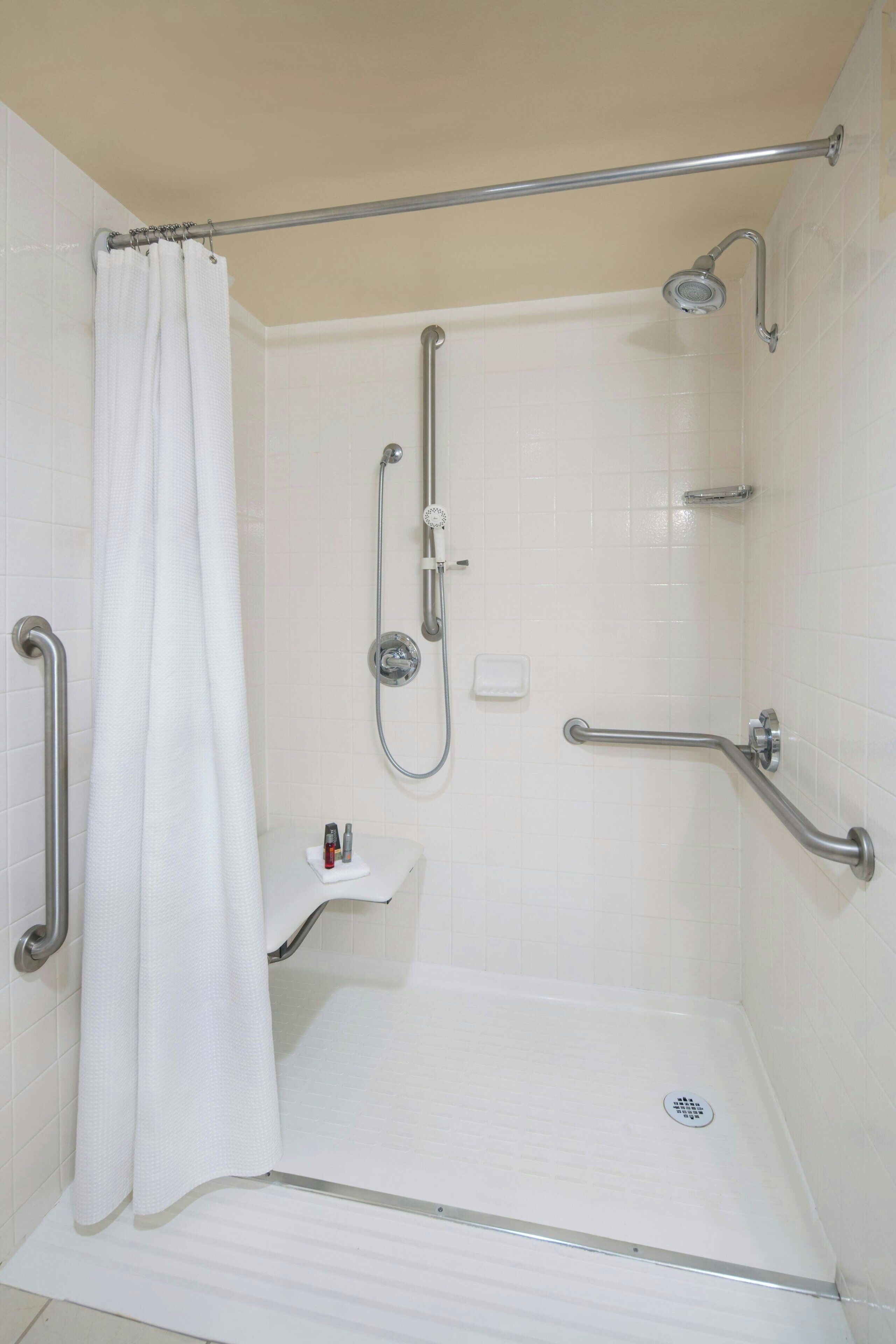 A walk-in shower with a grab bar, a showerhead, and a white tiled wall.
