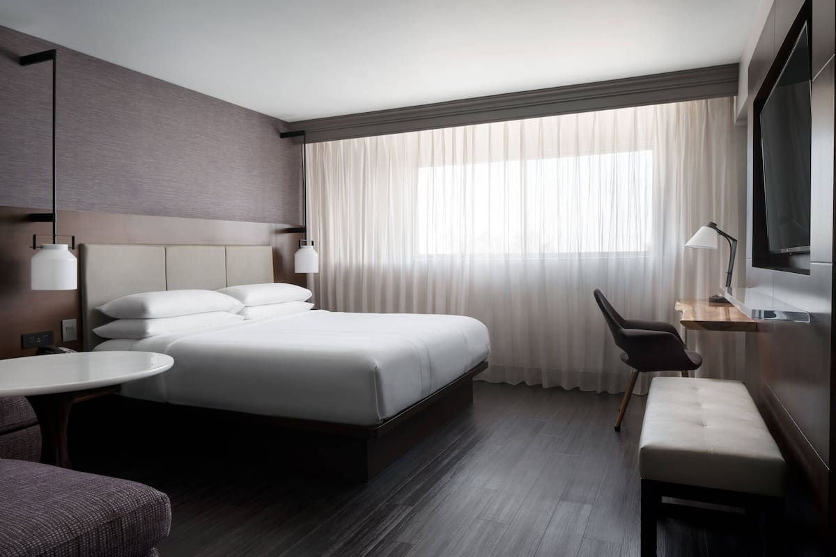 A modern hotel room with a large bed, a desk, a chair, and a TV.