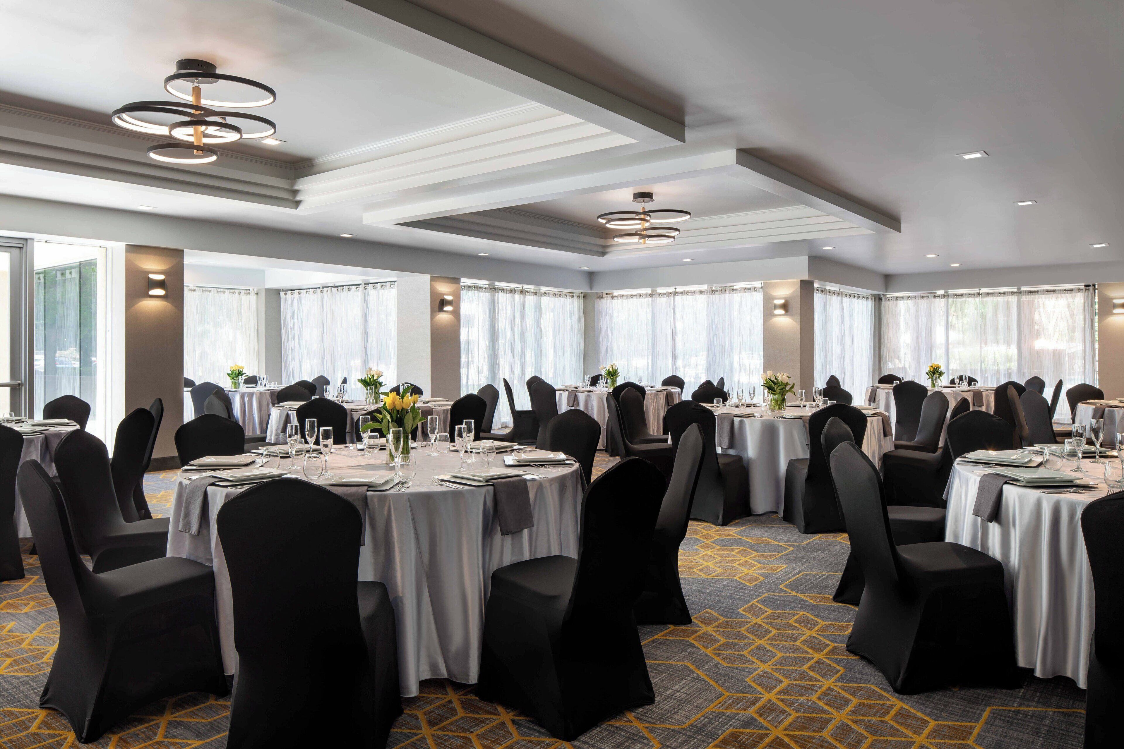 Un amplio salón de banquetes con mesas redondas, sillas negras y manteles blancos.
