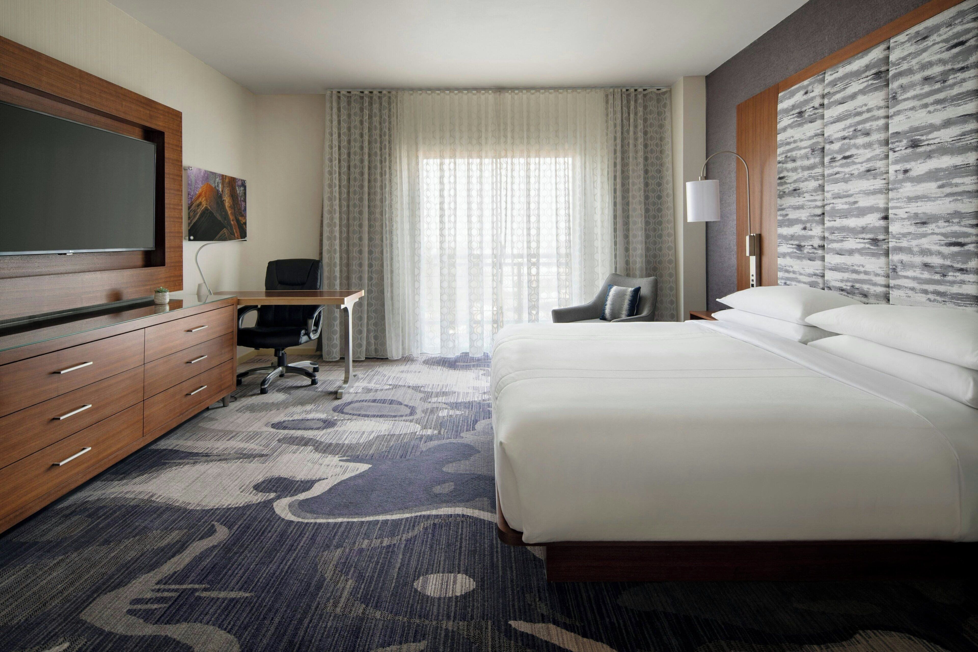 A hotel room with a bed, a desk, a chair, a television, and a window with curtains.