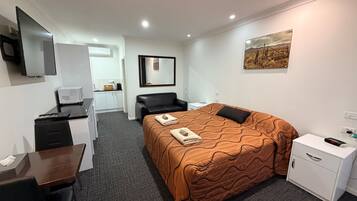 A hotel room with a bed, a desk, a chair, a TV, a painting, and a small table.