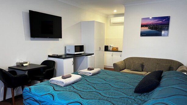 Ein Hotelzimmer mit einem Bett, einem Schreibtisch mit Computer, einem Sessel, einer Couch und einem Fernseher.