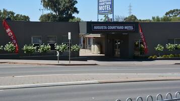L’extérieur du Augusta Courtyard Motel se distingue par un panneau indicateur bien visible, une entrée fermée par un portail et un espace paysager agrémenté de petites plantes.