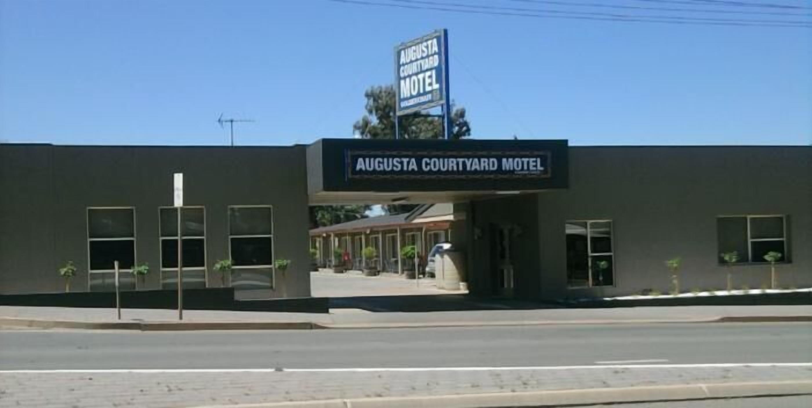 Exterior del Augusta Courtyard Motel, con un letrero visible, un estacionamiento y la entrada al edificio.