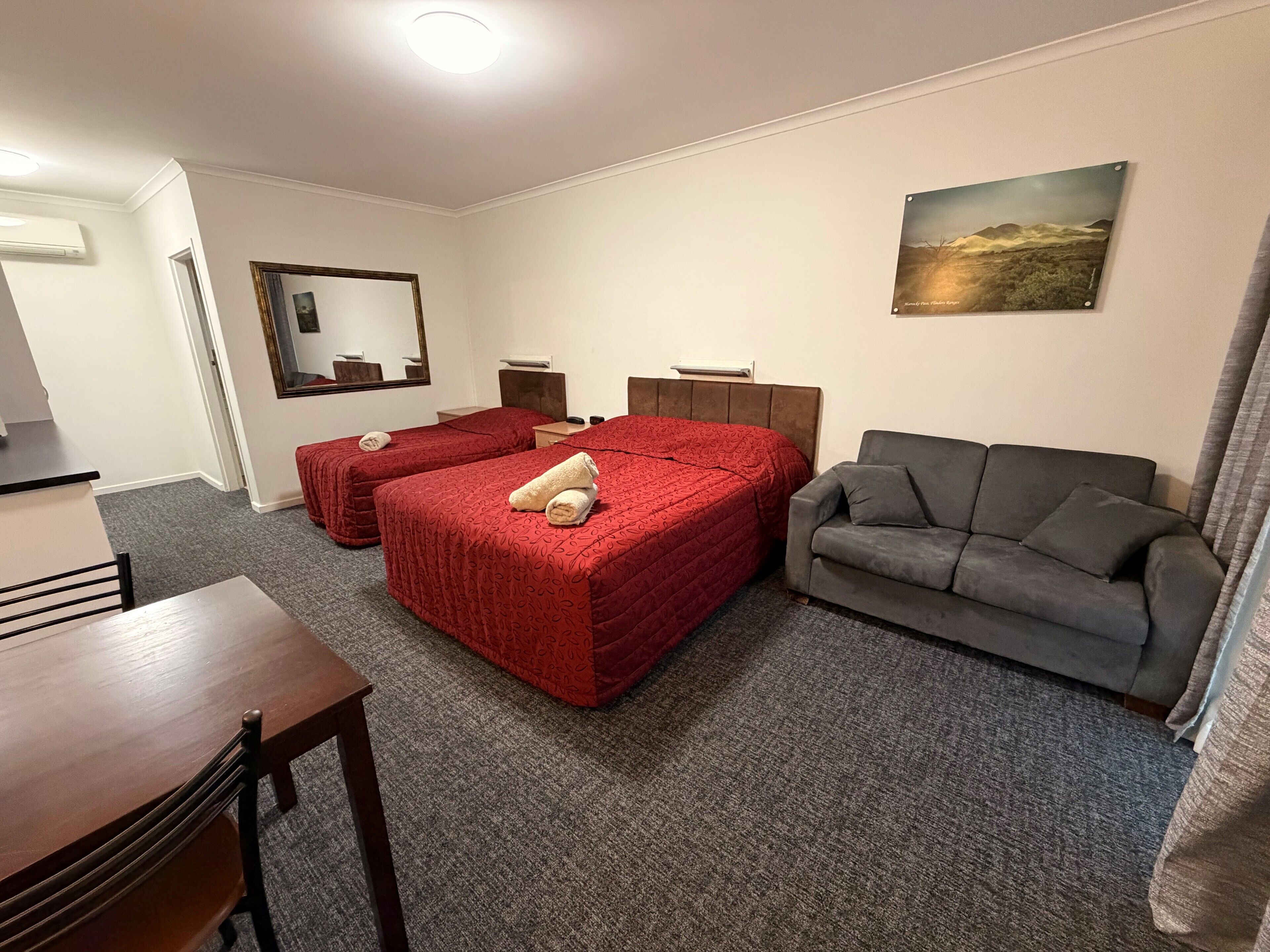 A hotel room with two beds, a sofa, a desk, and a mirror.