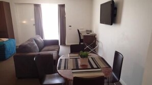 Ein kompakter Wohnbereich mit einer Couch, einem Esstisch mit Stühlen, einem an der Wand befestigten Fernseher und einem Fenster mit Vorhängen.