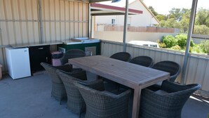 Eine Terrasse im Freien mit einem Holztisch, Korbstühlen, einem kleinen Kühlschrank und einer kompakten Küchenzeile.