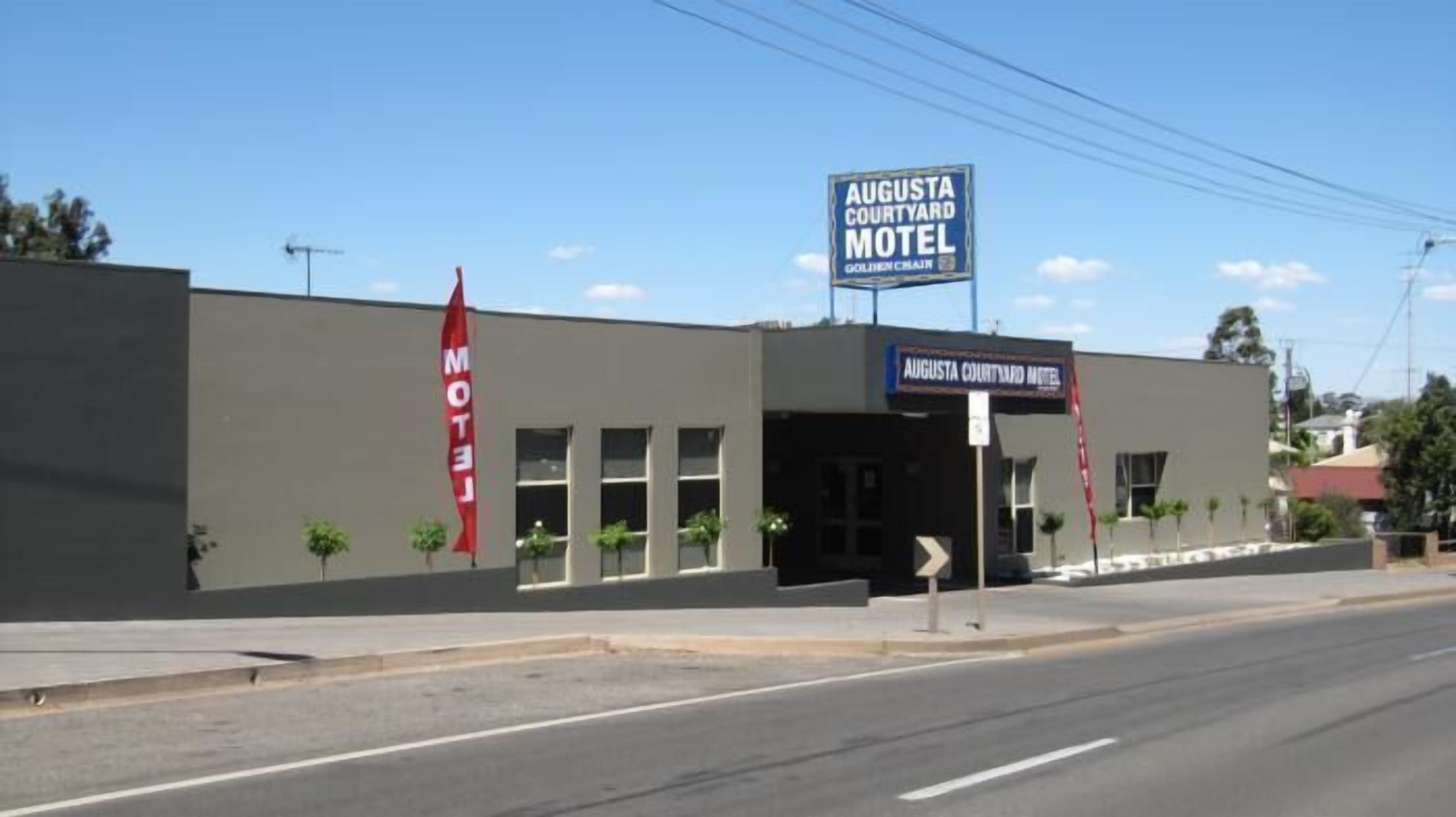 A motel with a sign reading "Augusta Courtyard Motel" and a red flag with "MOTEL" on it.