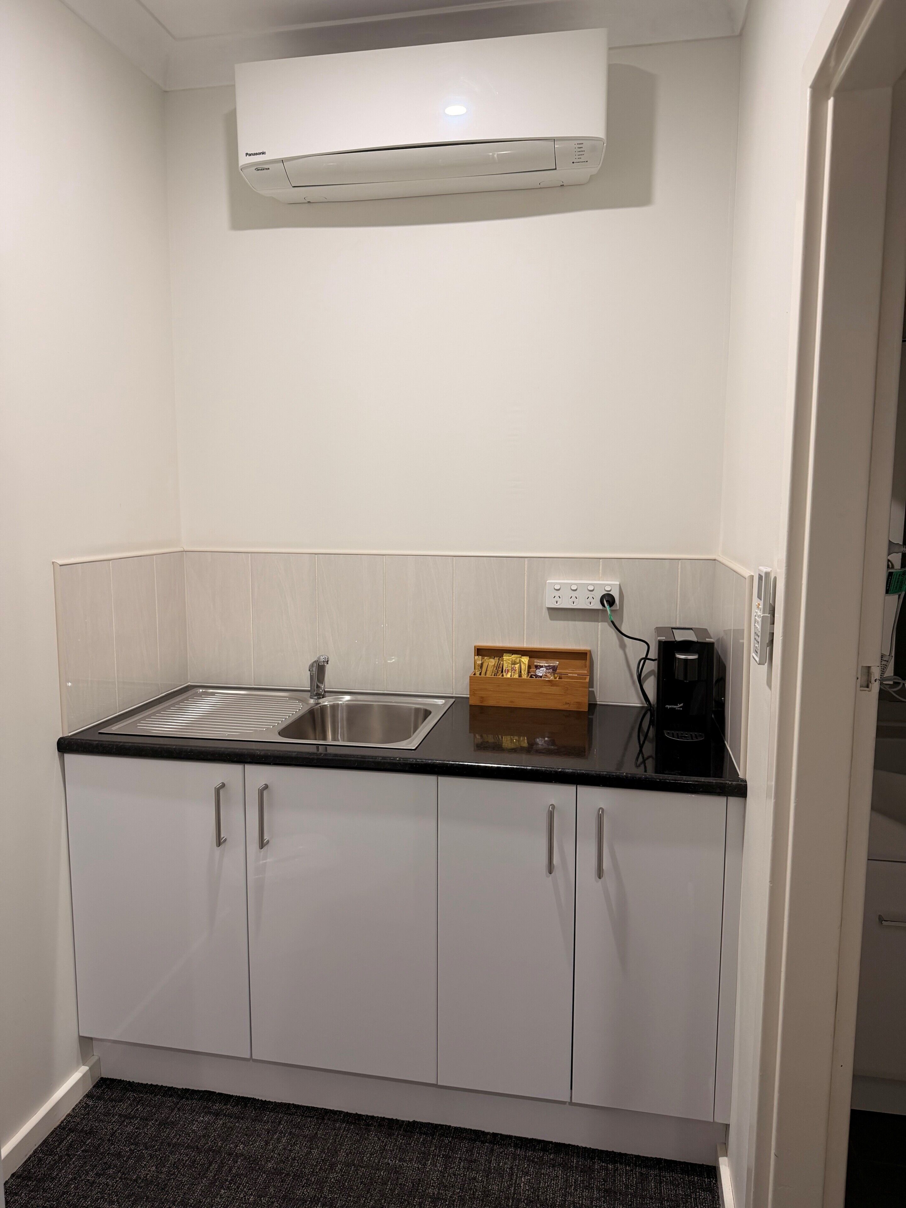 A compact kitchen with a built-in sink, a coffee maker, and a box of snacks on the countertop.