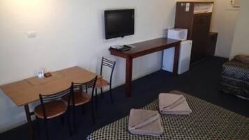 Quarto pequeno com uma cama, escrivaninha, cadeira, televisão e guarda-roupa.