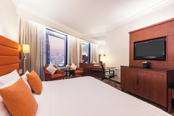 Une chambre d’hôtel avec un grand lit, un bureau, une télévision et une vue sur la ville par les fenêtres.