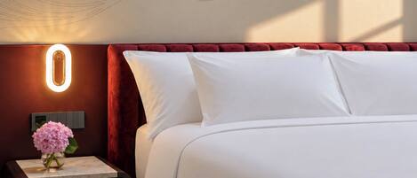 A hotel room with a bed, a nightstand, a vase with flowers, and a wall-mounted light fixture.