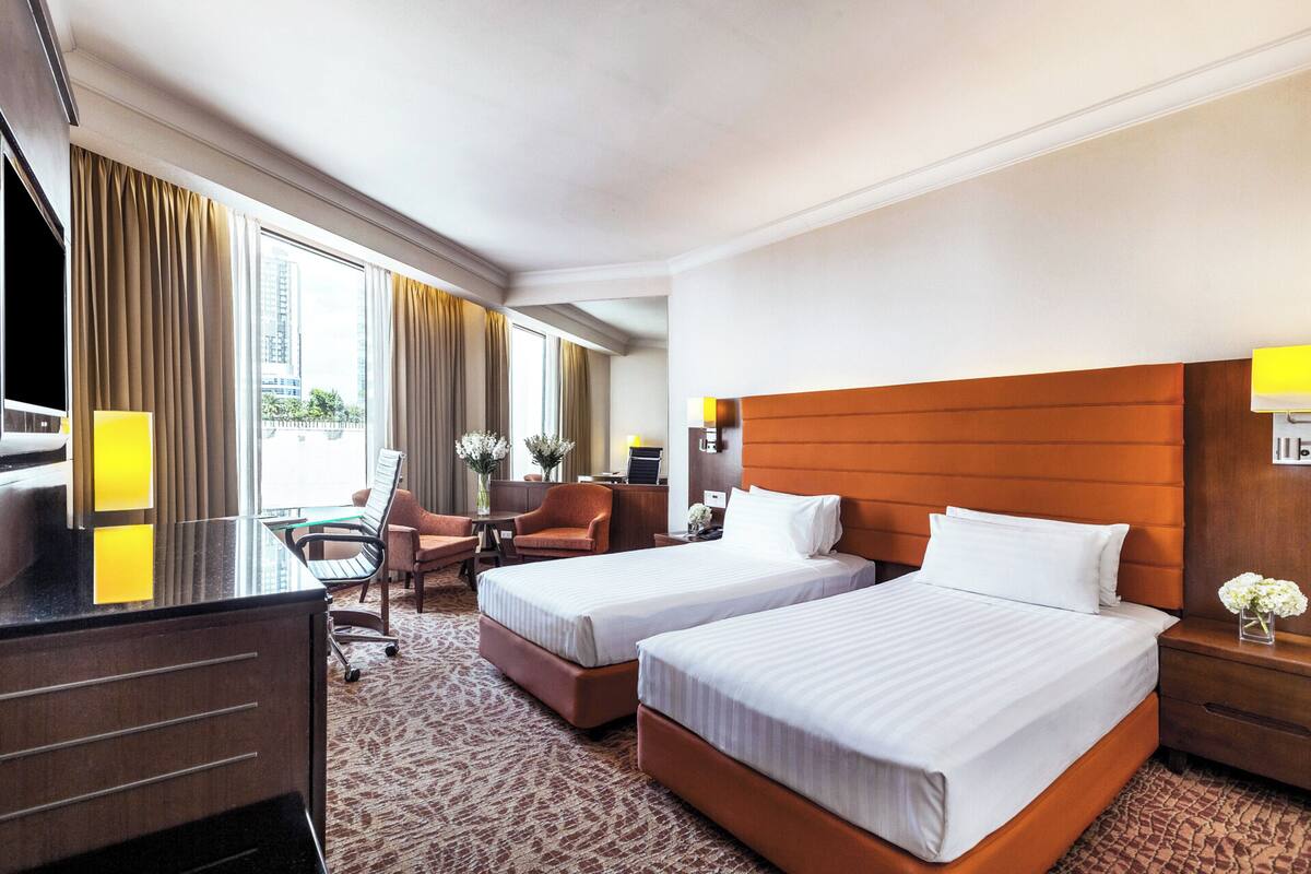 A hotel room with two beds, a desk, a chair, and a view of the city.