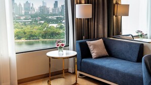 Une chambre d’hôtel moderne avec vue sur la ville, un canapé bleu, une table ronde dorée et une lampe.
