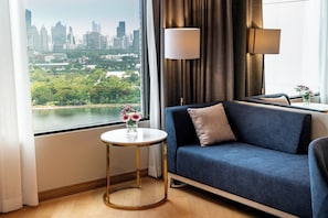 Une chambre d’hôtel moderne avec vue sur la ville, un canapé bleu, une table ronde dorée et une lampe.