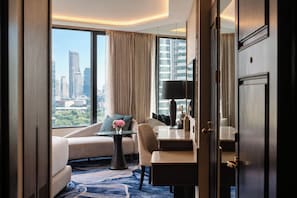 A hotel room with a city view, a sofa, a dining table, and a mirror.