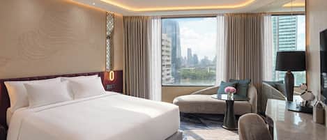 A hotel room with a large bed, a desk with a chair, a view of the cityscape, and a modern ceiling design.