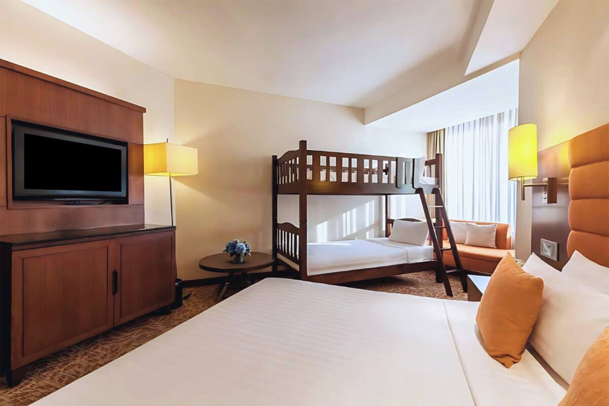 A hotel room with a bunk bed, a flat bed, a television, a desk, and a lamp.
