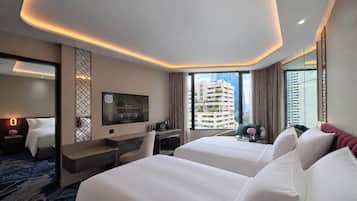A hotel room with two beds, a desk, a TV, and a city view.