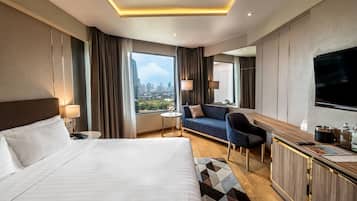 A hotel room with a large bed, a sofa, a desk with a TV, and a city view.