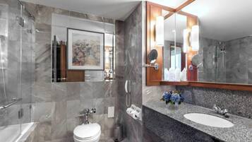 A modern bathroom with a marble shower, a toilet, a sink with a granite countertop, and a large mirror.