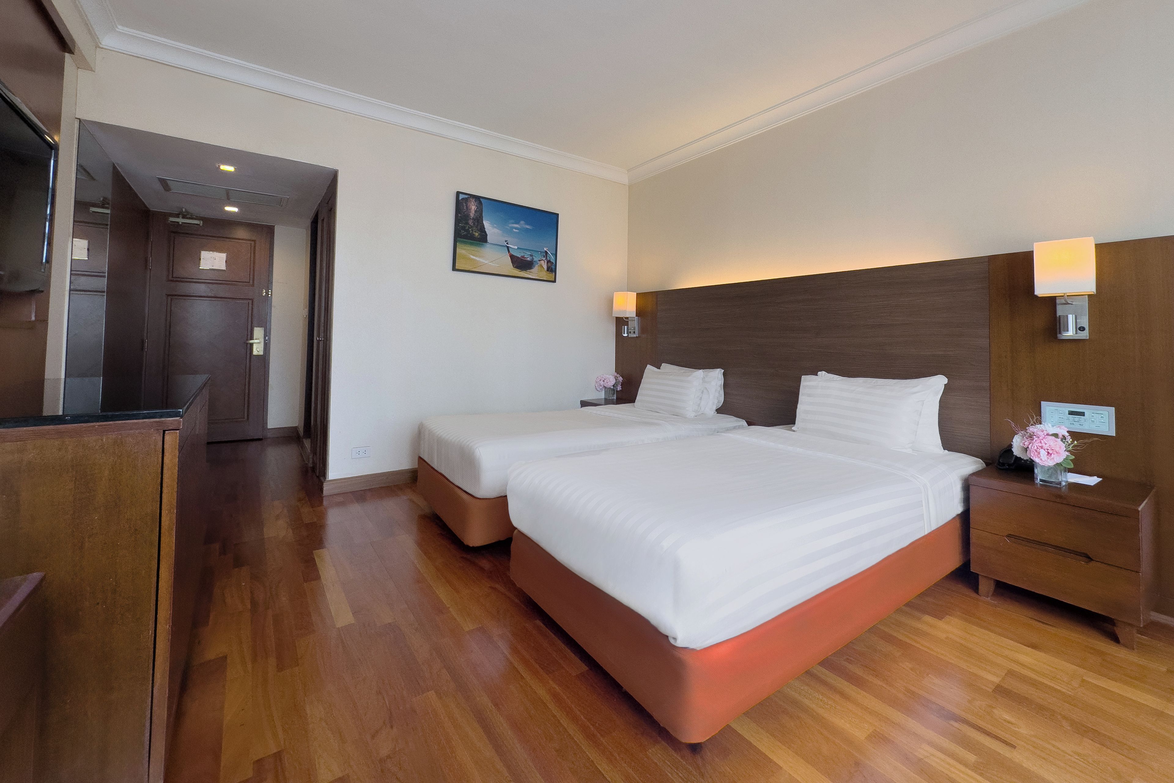 A hotel room with a large bed, a wooden nightstand, a desk, and a painting on the wall.