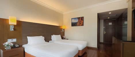 Habitación de hotel con dos camas, suelo de madera, una mesita de noche con teléfono, lámpara y un cuadro en la pared.