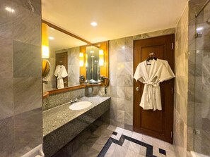 A bathroom with a marble sink, a large mirror, and a robe hanging on the door.