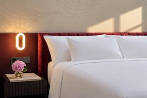 Habitación de hotel con cama, mesita de noche, un florero y una lámpara de pared.