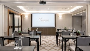 Ein Konferenzraum mit Tischen, Stühlen und einer Projektionsleinwand, die 'Rembrandt Hotel Bangkok' zeigt.