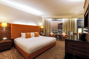 A hotel room with a large bed, a desk, two chairs, and a view of the cityscape. - Rembrandt Hotel Bangkok (Bangkok)