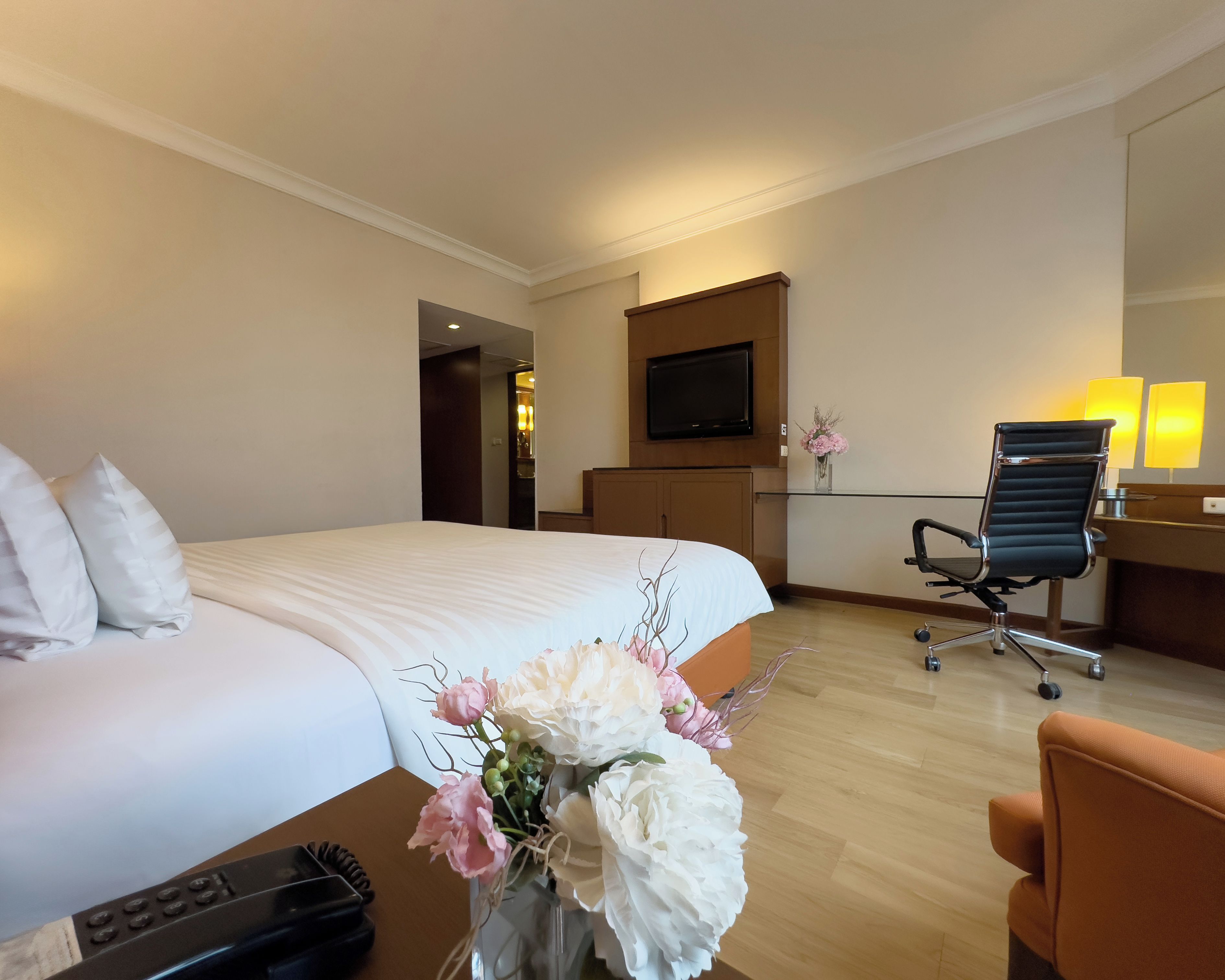 Une chambre d’hôtel avec un grand lit, un bureau avec une chaise, un téléviseur fixé au mur et un vase rempli de fleurs sur le bureau.