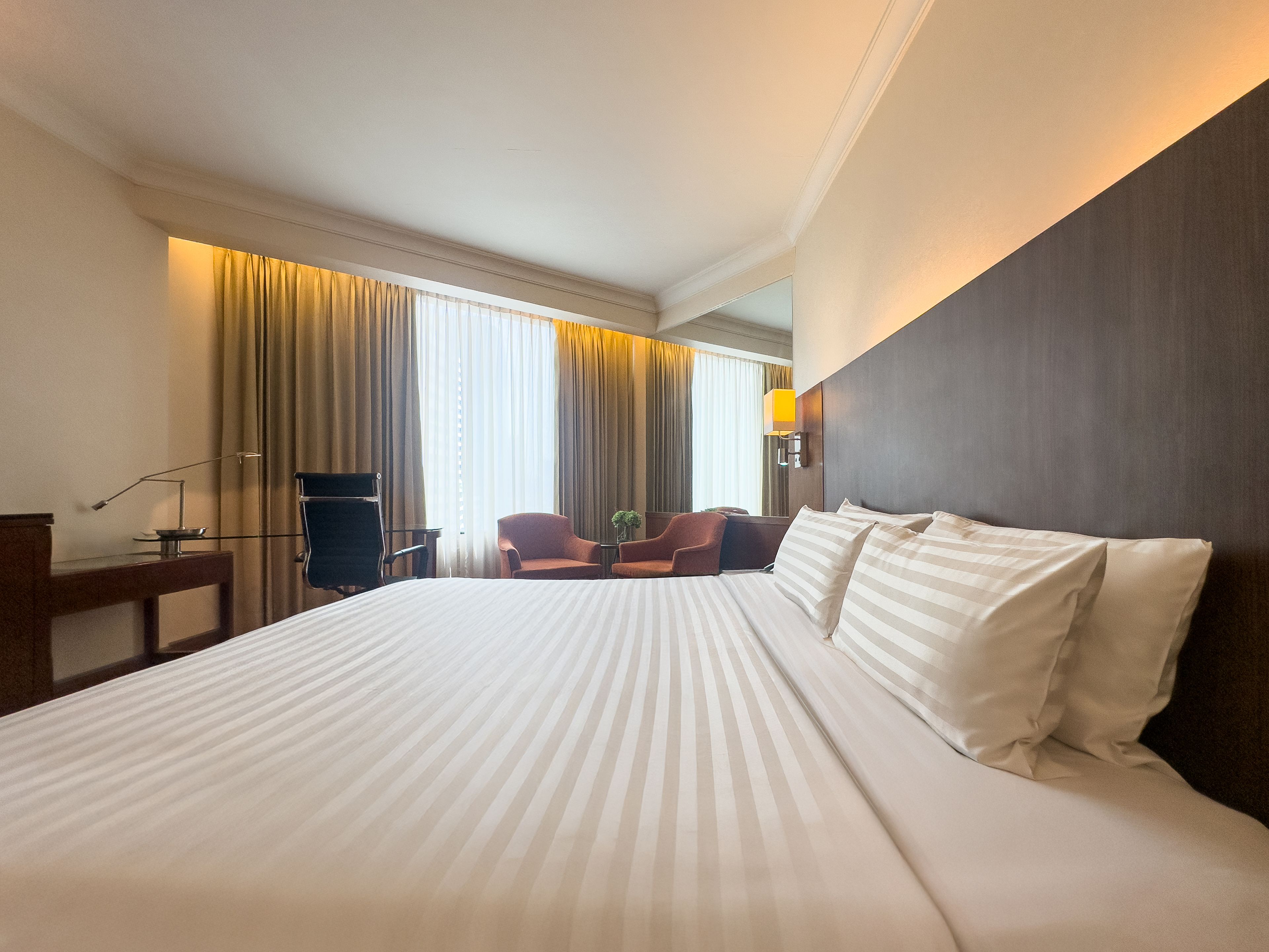 A hotel room with a large bed, a desk, a chair, and a small table.