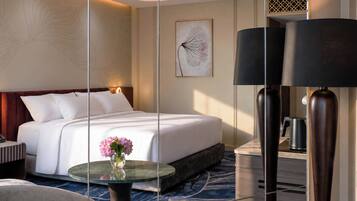 A hotel room with a large bed, a glass coffee table with flowers, a modern lamp, and a framed artwork on the wall.