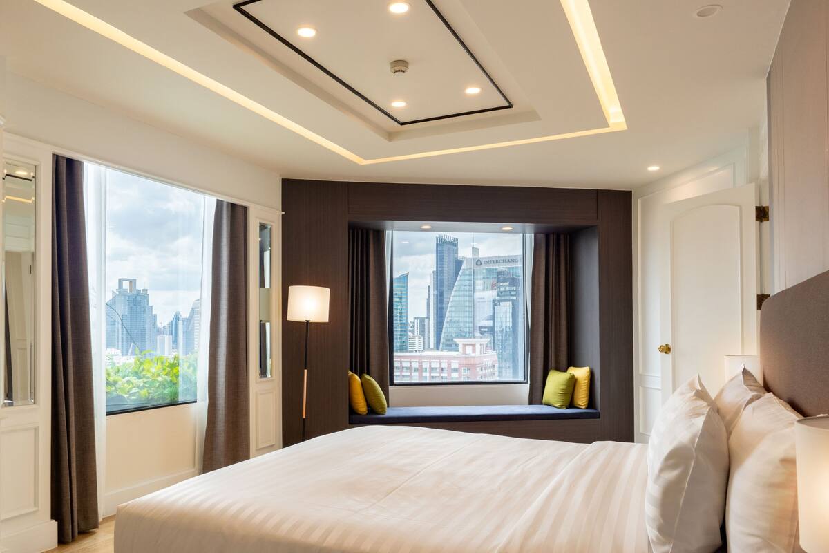 A modern hotel room with a large bed, a window with a city view, and a ceiling with recessed lighting.