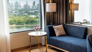 Habitación de hotel moderna con vista a la ciudad, un sofá azul, una mesa redonda dorada y una lámpara.