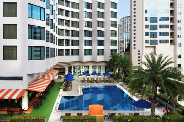 Relax by the rectangular pool surrounded by lounge chairs and umbrellas, set amidst lush greenery and large windows.