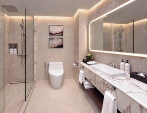 Un baño moderno con ducha envuelta en vidrio, inodoro, lavamanos con encimera de mármol y un espejo grande.