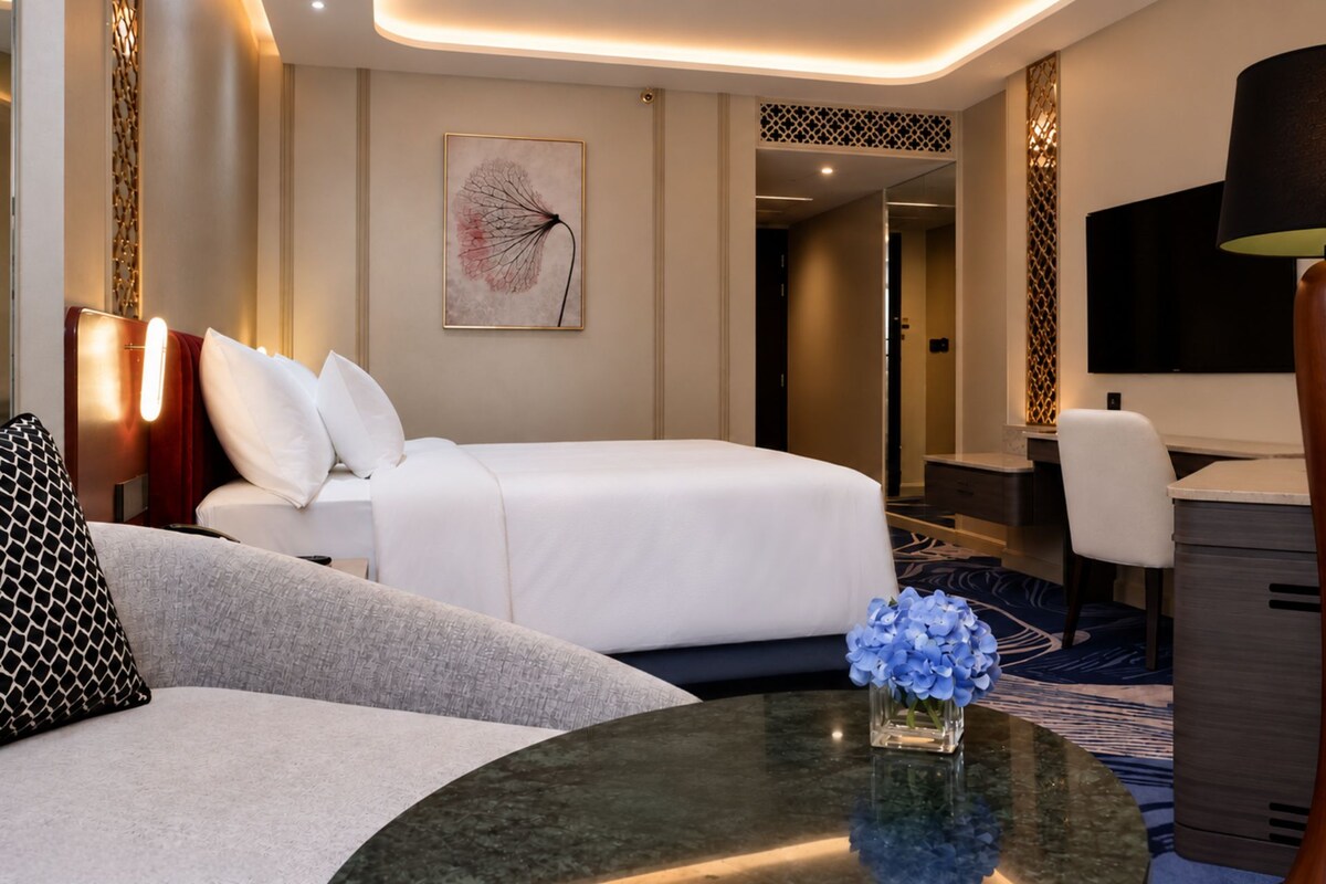 Een hotelkamer met een bed, een bureau, een stoel, een lamp en een vaas met bloemen.