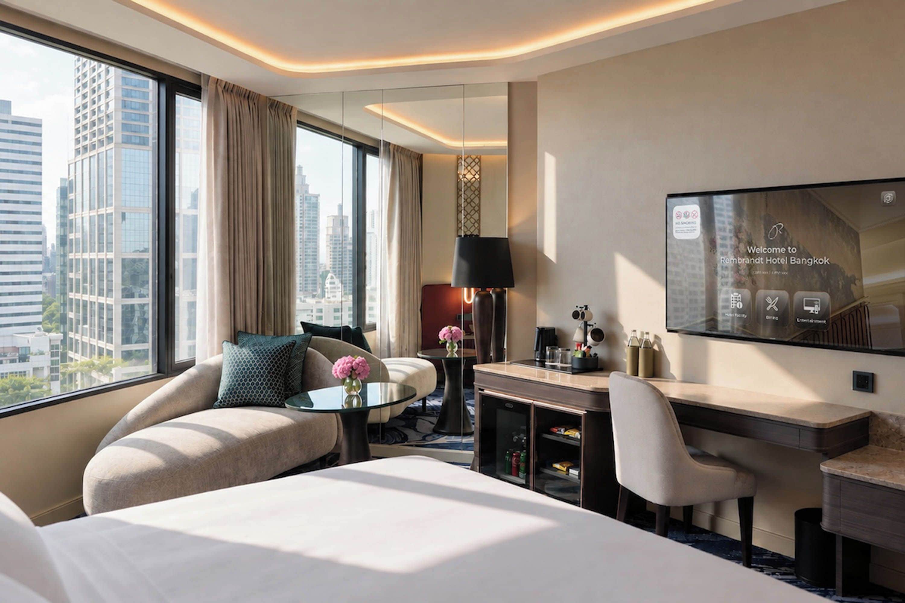 A modern hotel room with a bed, a desk, a chair, a TV, and a view of the cityscape.