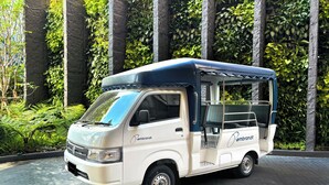 Een witte en blauwe bus met 'Rembrandt' branding geparkeerd voor een muur met weelderige groene begroeiing.