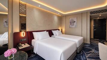 A hotel room with two beds, a desk, a phone, a vase with flowers, and artwork on the walls.