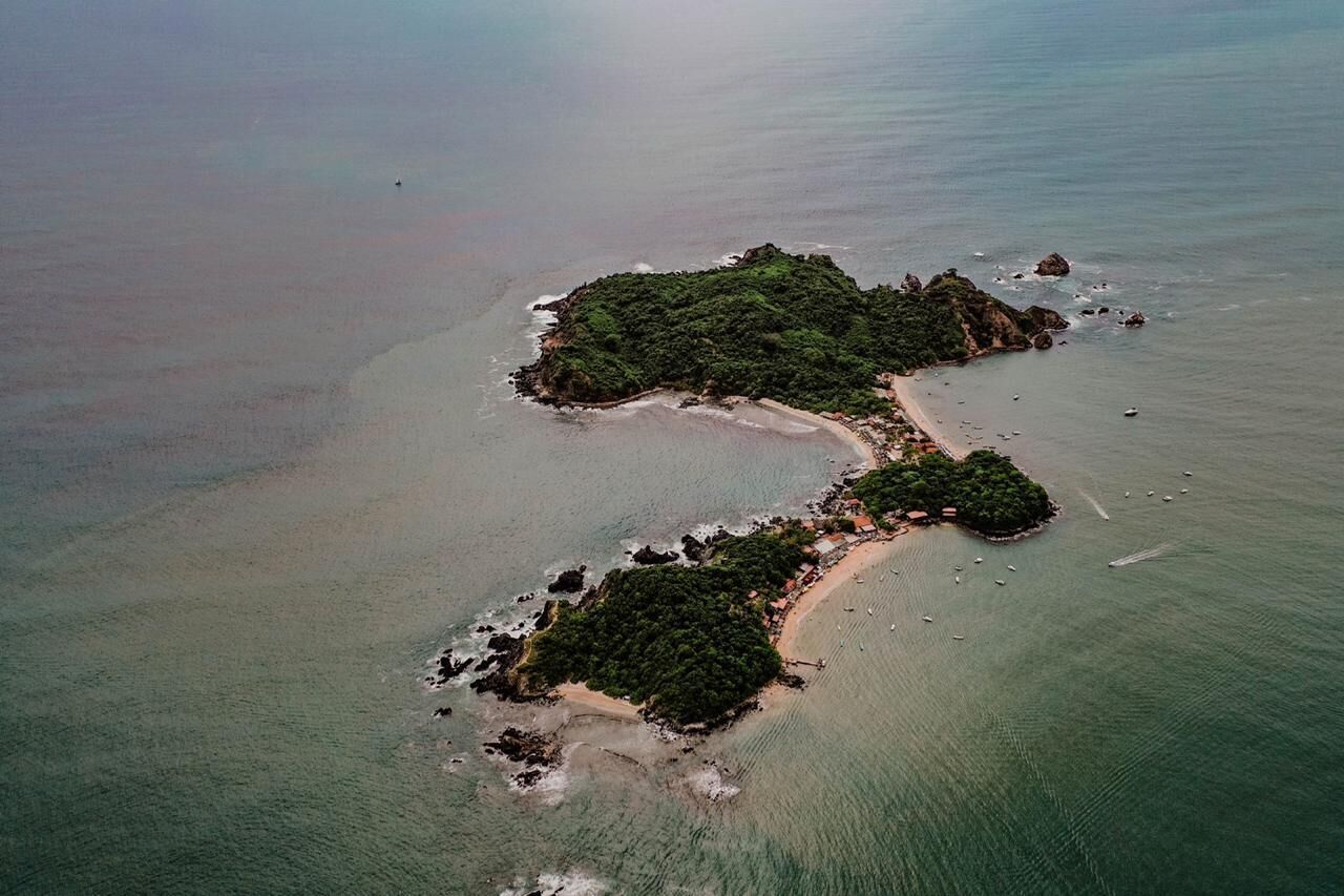 An aerial view of a small, green island with a narrow beach.