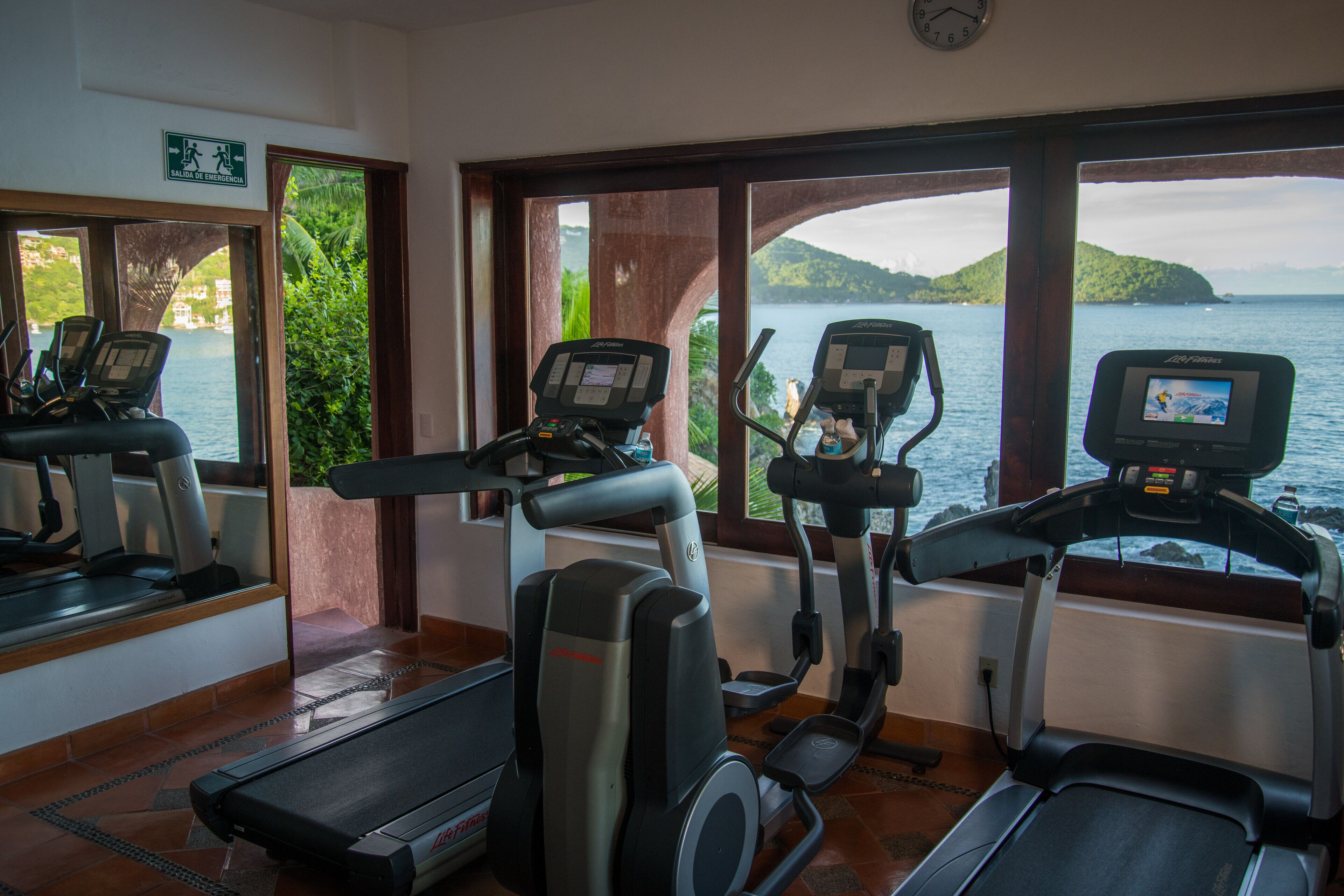 A fitness room with treadmills and exercise bikes, large windows with a view of the sea and hills.